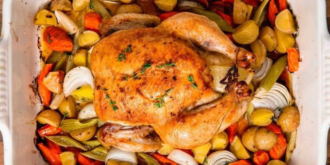 En hel kylling i ovnen på en seng av grønnsaker